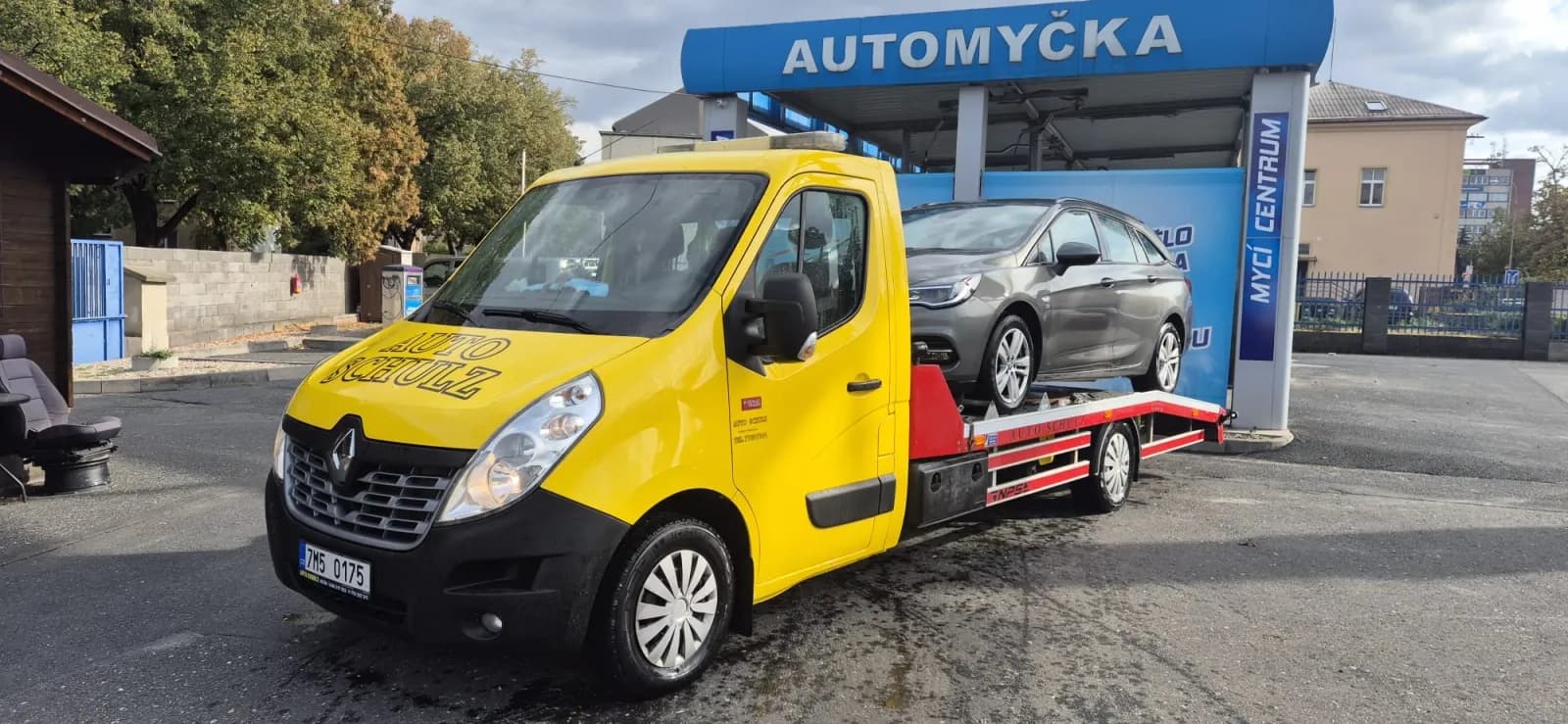 Žlutý odtahový vůz Auto Schulz s naloženým osobním autem na plošině